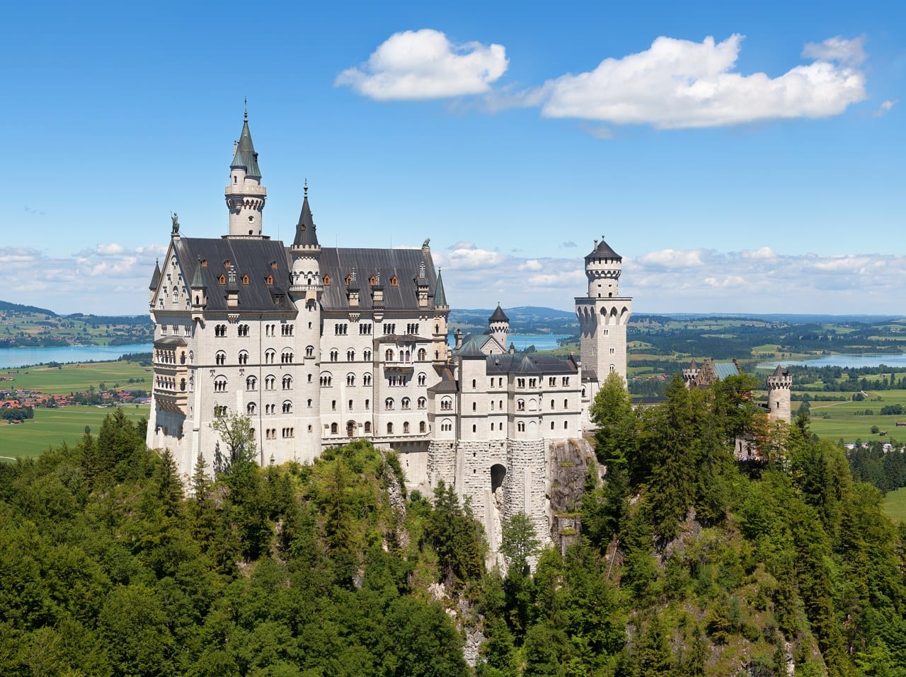 Neuschwanstein Castle 1 Neuschwanstein Castle from the south, its five-storey Palas and round-arched arcaded windows above the wooded crag, with the Alpine foreland and the lakes beyond