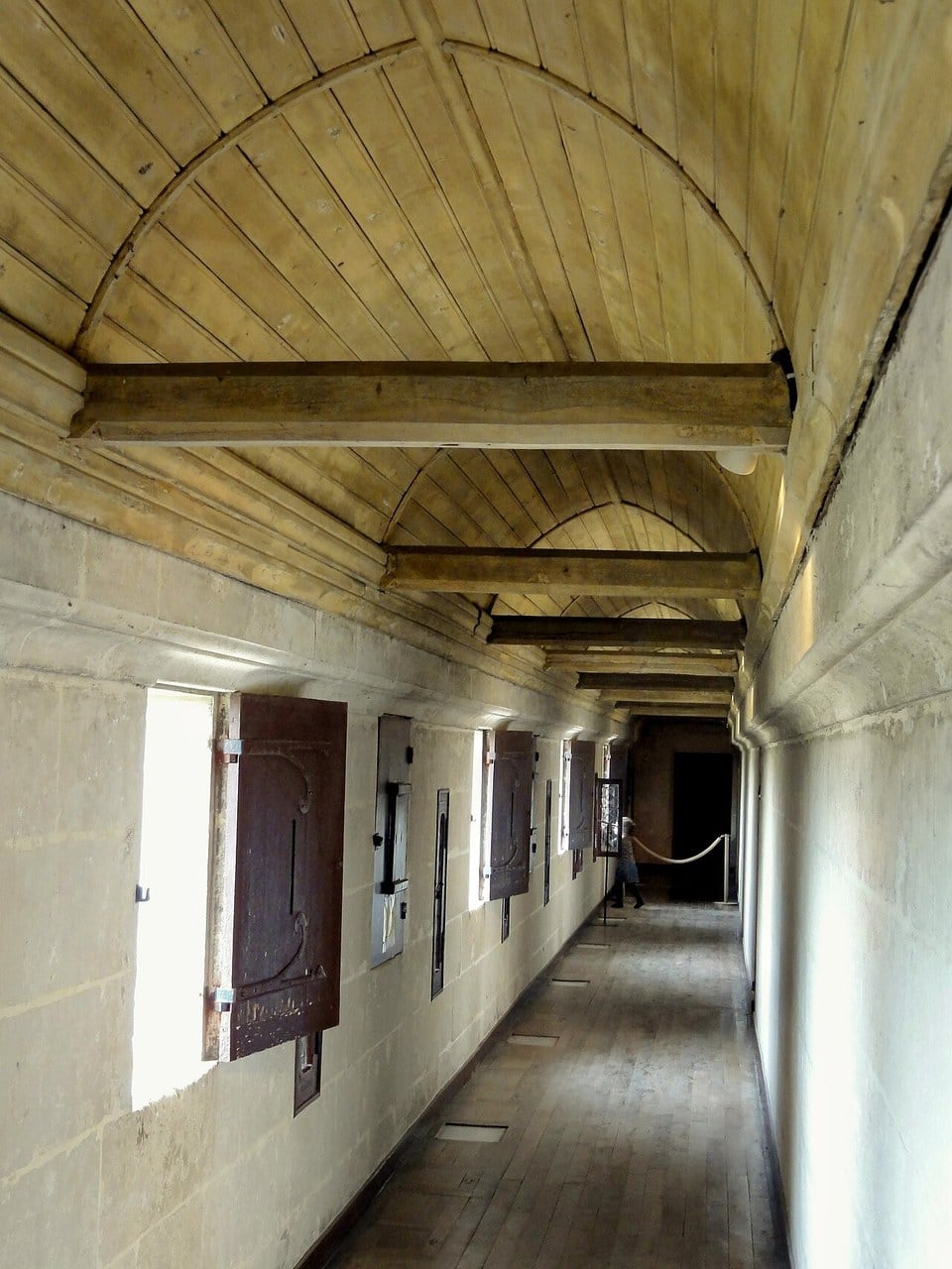 A long roofed gallery at Pierrefonds with a plank floor; the left-hand outer wall carries hinged timber shutters and narrow vertical slits, and a row of rectangular panels is set into the floor along its foot. A long roofed gallery at Pierrefonds with a plank floor; the left-hand outer wall carries hinged timber shutters and narrow vertical slits, and a row of rectangular panels is set into the floor along its foot.