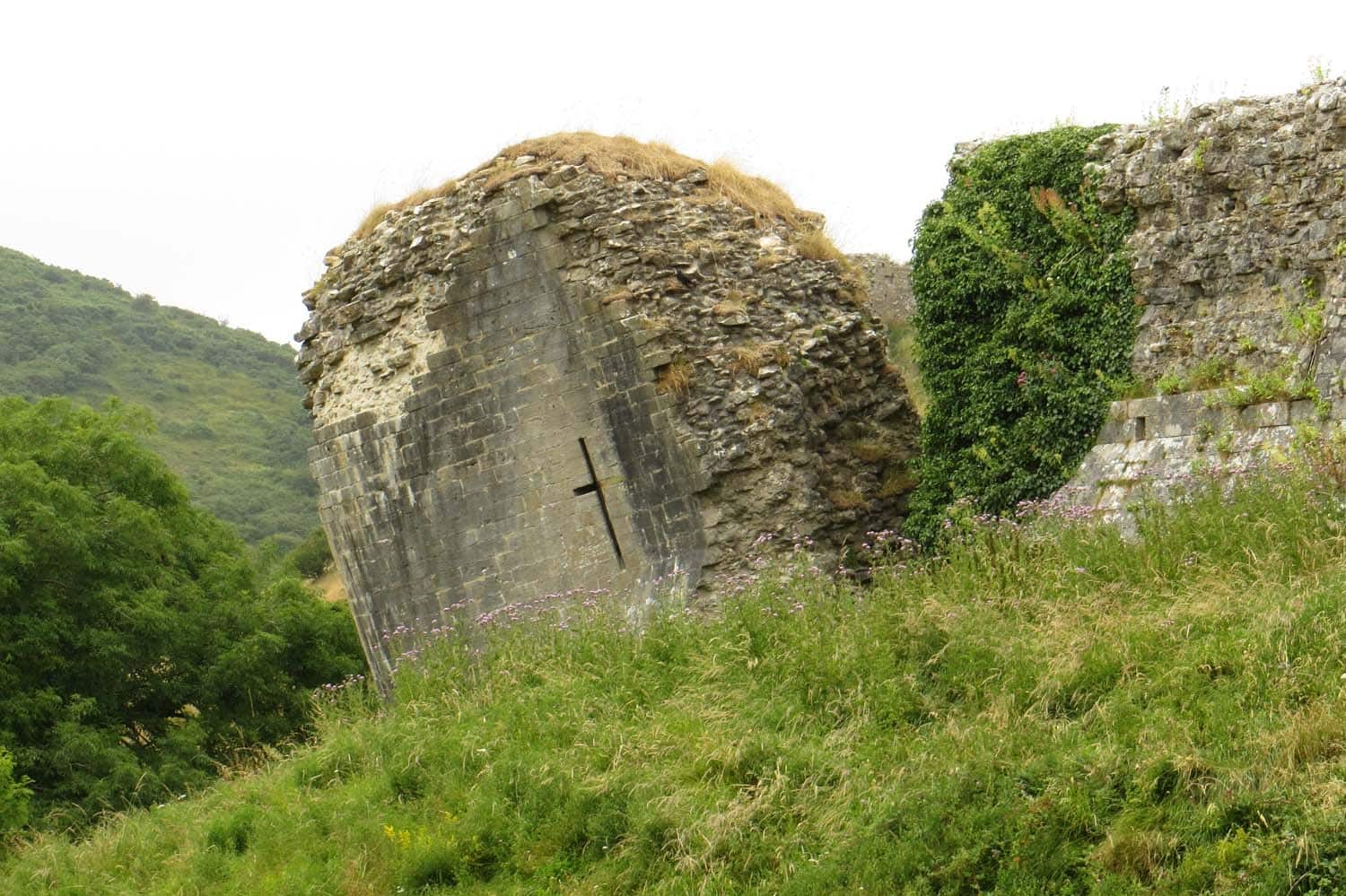 A ruined stone wall at Corfe Castle where smooth dressed-stone facing survives on the left, cut by a narrow cross-shaped arrow loop, while the rough rubble-and-mortar core is exposed at the ragged break where the outer facing has broken away. Ruined wall at Corfe Castle: dressed ashlar facing over an exposed rubble-and-mortar core, with a cross-shaped arrow loop.