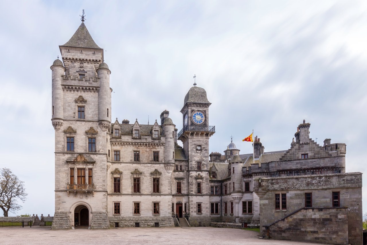 The castle's north entrance front across a gravel forecourt: a square four-stage tower with a round-headed entrance arch at its base, corbelled round angle turrets with conical caps, and a corbelled square caphouse under a steep pyramidal roof, with the clock tower and a flying Sutherland flag to the right. The castle's north entrance front across a gravel forecourt: a square four-stage tower with a round-headed entrance arch at its base, corbelled round angle turrets with conical caps, and a corbelled square caphouse under a steep pyramidal roof, with the clock tower and a flying Sutherland flag to the right.