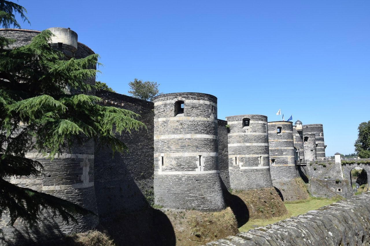 A receding line of massive round towers along the outer ditch at the château of Angers, built in bands of dark and pale stone, every one of them flat-topped.
