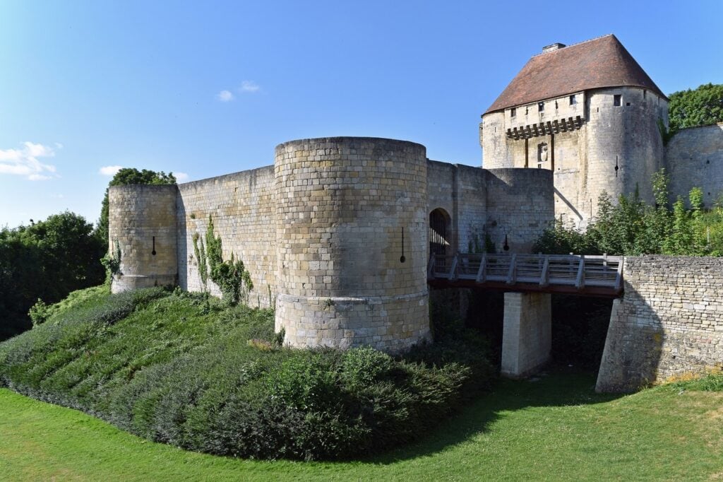 Château de Caen 7 The barbican of the Porte des Champs at the Château de Caen in low sunlight, with a timber footbridge and the roofed gate tower carrying a timber hoarding behind it.