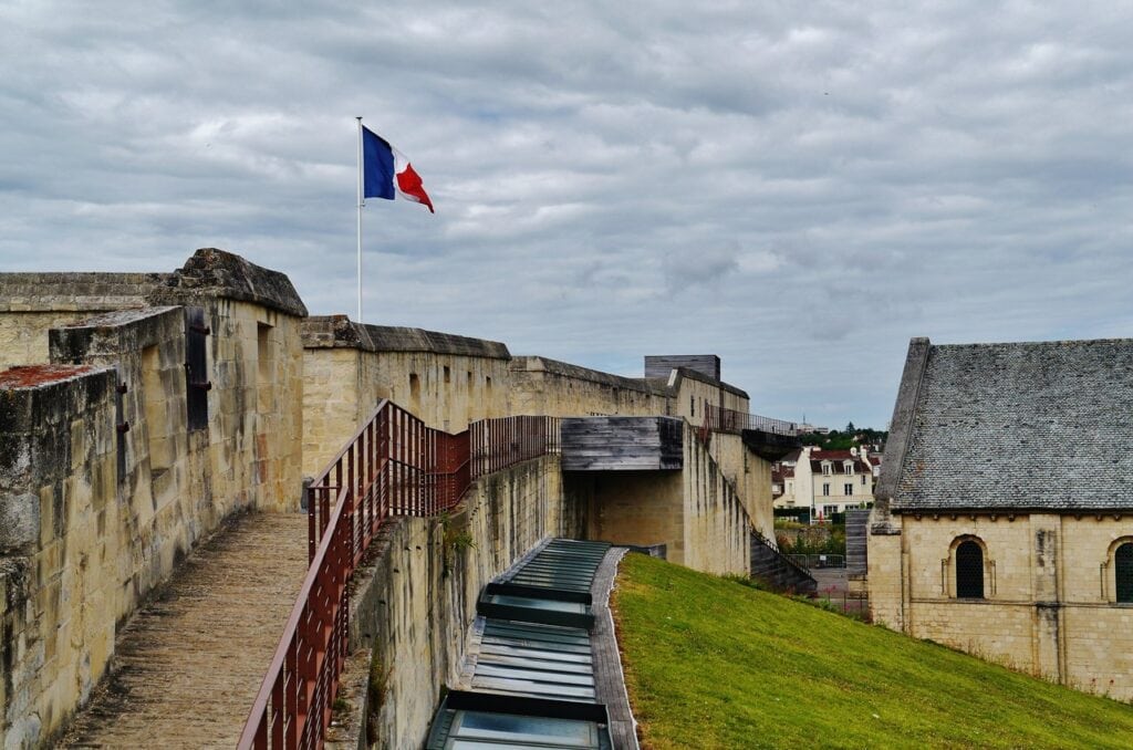 Château de Caen 6 The rampart wall walk on the northwest curtain of the Château de Caen, with a French flag and glazed museum rooflights in the ditch below.