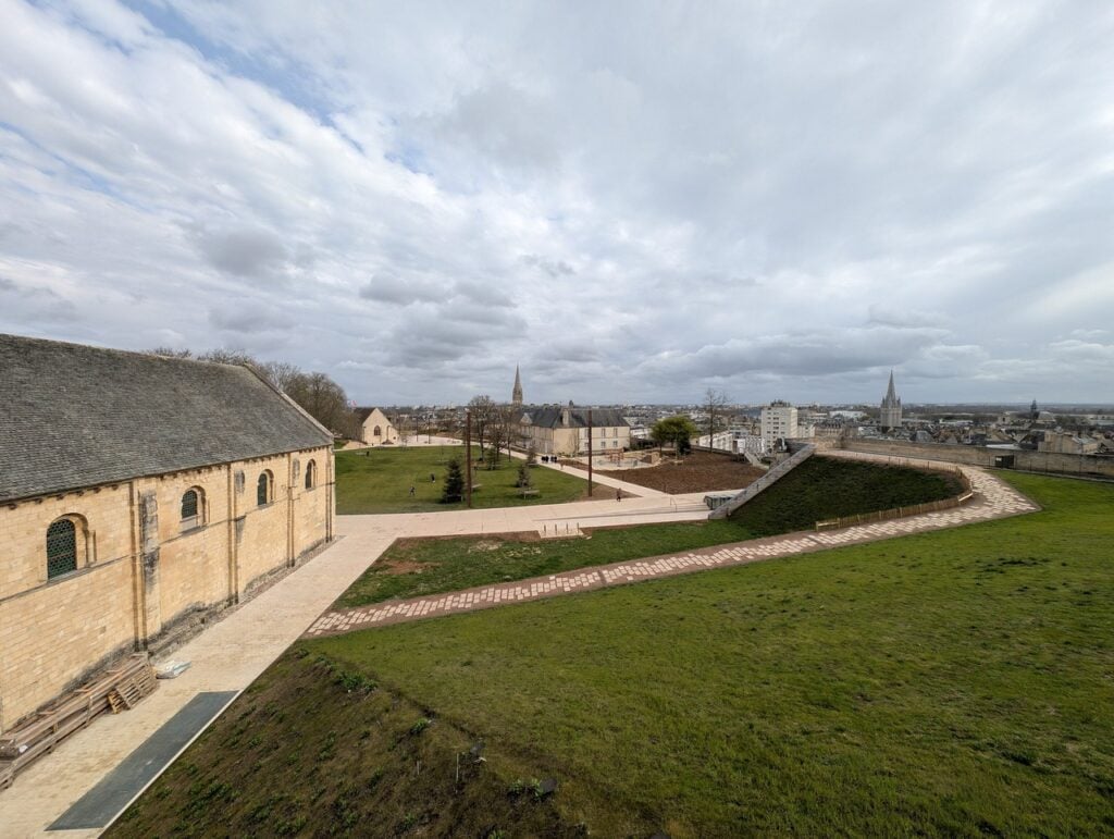 Château de Caen 8 A wide view across the grassed bailey of the Château de Caen from the artillery terrace, the Salle de l'Échiquier at left and the spire of Saint-Pierre rising beyond the curtain wall.