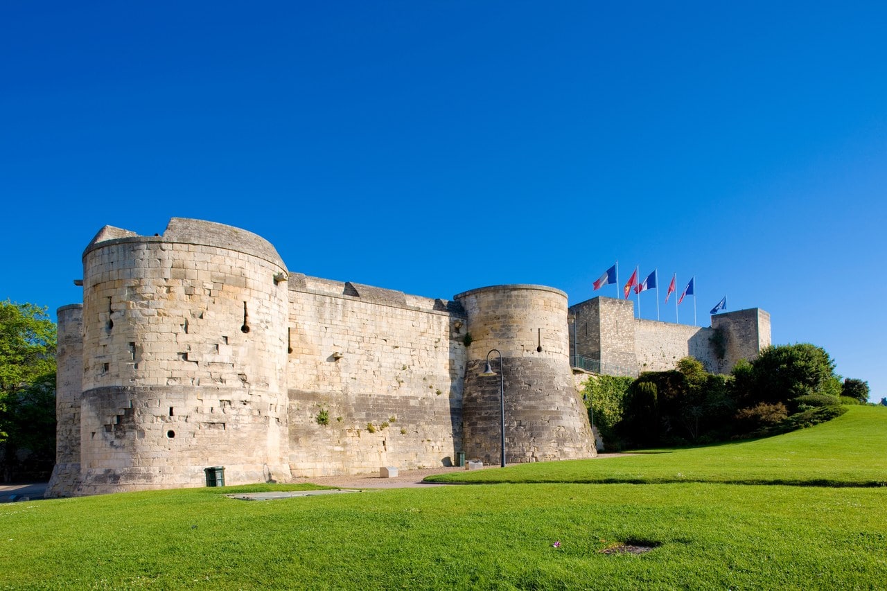 Two round mural towers projecting from the ashlar curtain wall of the Château de Caen, seen from the grass below, with flags on the rampart above. Two round mural towers projecting from the ashlar curtain wall of the Château de Caen, seen from the grass below, with flags on the rampart above.