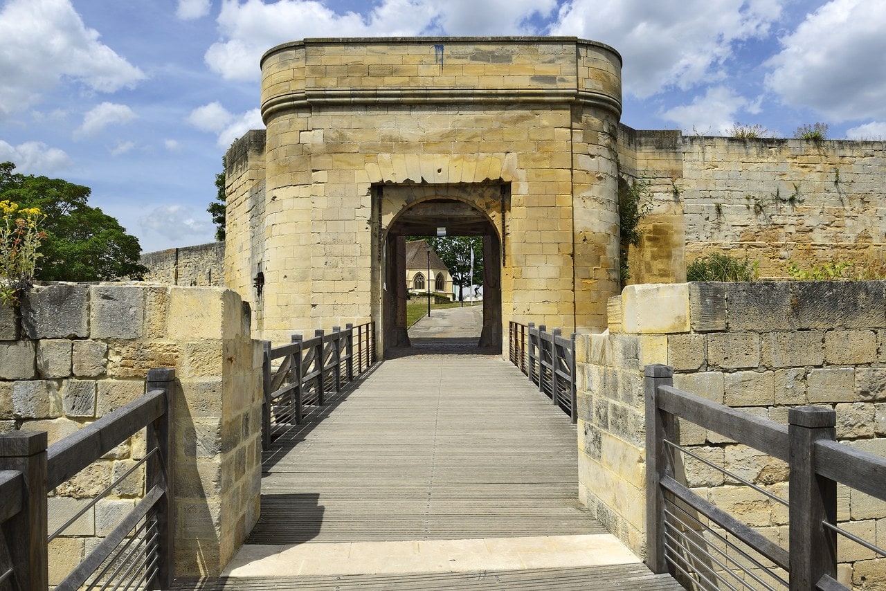 View along a timber bridge and through the arched gateway of the Porte Saint-Pierre at the Château de Caen, with the church of Saint-Georges visible inside the enclosure beyond. View along a timber bridge and through the arched gateway of the Porte Saint-Pierre at the Château de Caen, with the church of Saint-Georges visible inside the enclosure beyond.