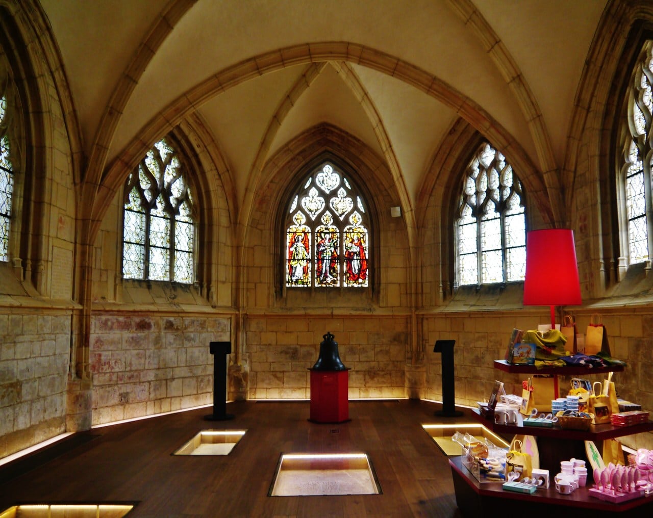 The rib-vaulted chancel of the church of Saint-Georges at the Château de Caen, with traceried windows, a figured stained-glass window, uplit floor slabs and display stands to the right. The rib-vaulted chancel of the church of Saint-Georges at the Château de Caen, with traceried windows, a figured stained-glass window, uplit floor slabs and display stands to the right.