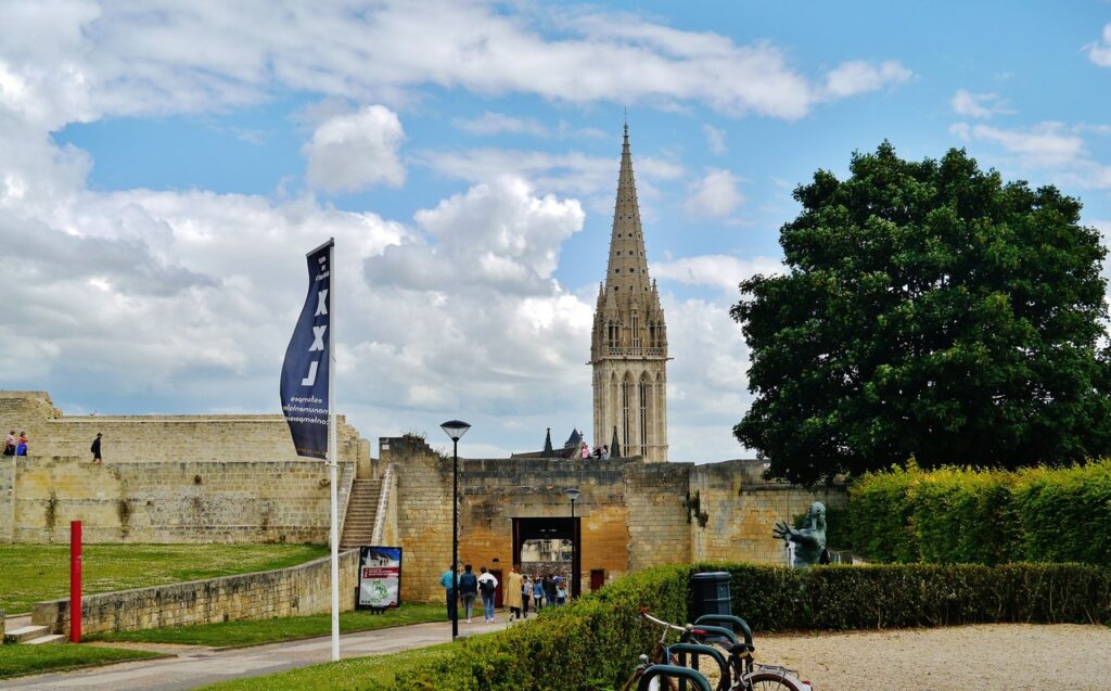 Château de Caen 12 The inner face of the Porte Saint-Pierre at the Château de Caen seen from within the enclosure, with steps up to the rampart and the spire of the church of Saint-Pierre beyond.