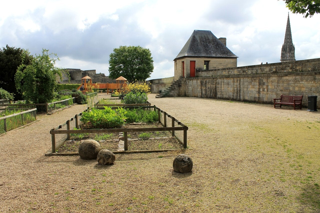 Railed planting beds of the jardin des Simples at the Château de Caen, with three stone cannonballs on the gravel in the foreground and a small roofed pavilion against the rampart wall behind. Railed planting beds of the jardin des Simples at the Château de Caen, with three stone cannonballs on the gravel in the foreground and a small roofed pavilion against the rampart wall behind.