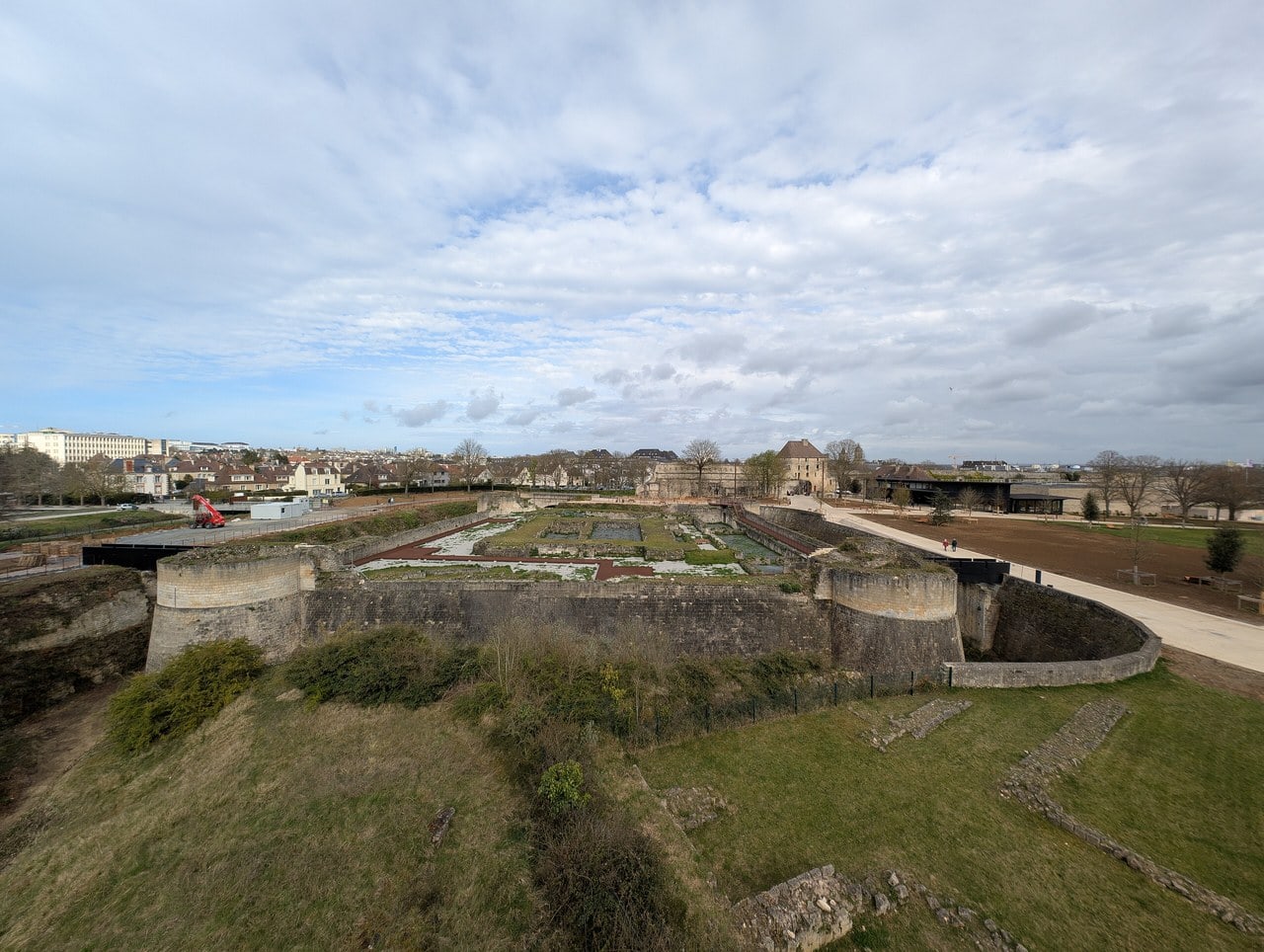The donjon site at the Château de Caen seen from above, showing the rectangular chemise wall with round corner turrets, a dry rock-cut moat in front of it, and low footings of the great tower laid out in the grass within. The donjon site at the Château de Caen seen from above, showing the rectangular chemise wall with round corner turrets, a dry rock-cut moat in front of it, and low footings of the great tower laid out in the grass within.