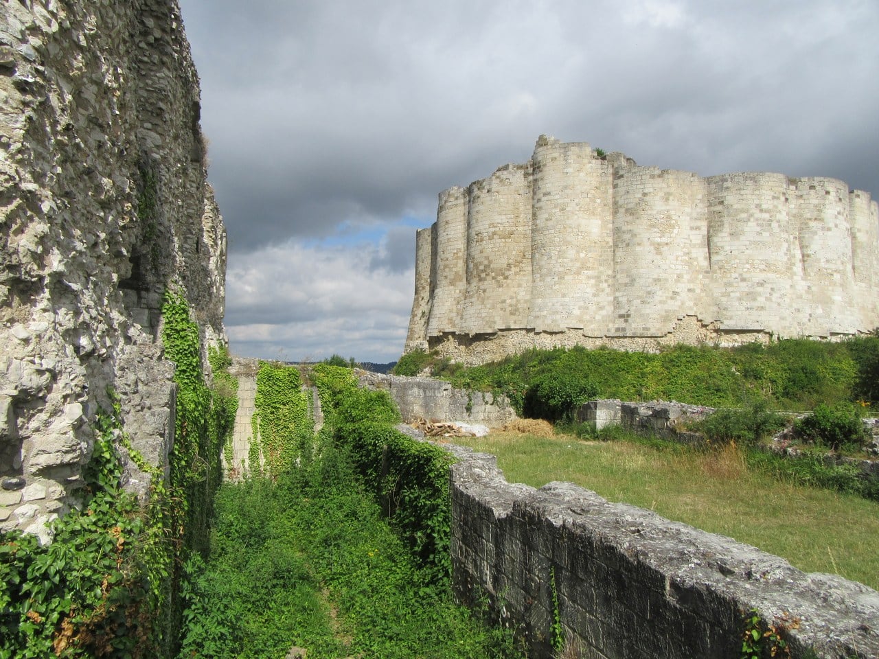 Château Gaillard's inner curtain seen from the ditch, its outer face formed of a continuous series of shallow cylinder segments separated by narrow strips of wall, with an ivy-covered rubble wall in the left foreground. Château Gaillard's inner curtain seen from the ditch, its outer face formed of a continuous series of shallow cylinder segments separated by narrow strips of wall, with an ivy-covered rubble wall in the left foreground.
