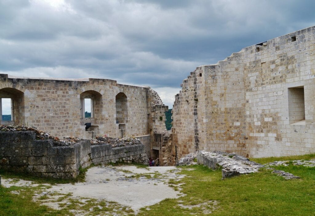 Château Gaillard 11 Ruined ranges inside Château Gaillard, a wall of round-headed openings at ground level and square windows above, standing on grass and bare chalk under a heavy sky.