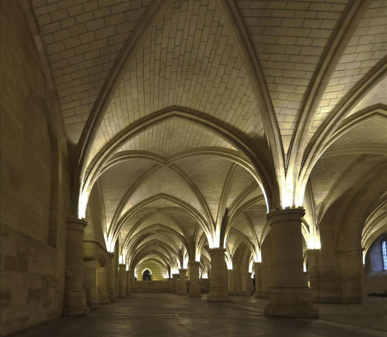 A vast vaulted stone room in four aisles: rows of stout round piers carry rib vaults, and the floor is bare stone with nothing standing on it. A vast vaulted stone room in four aisles: rows of stout round piers carry rib vaults, and the floor is bare stone with nothing standing on it.