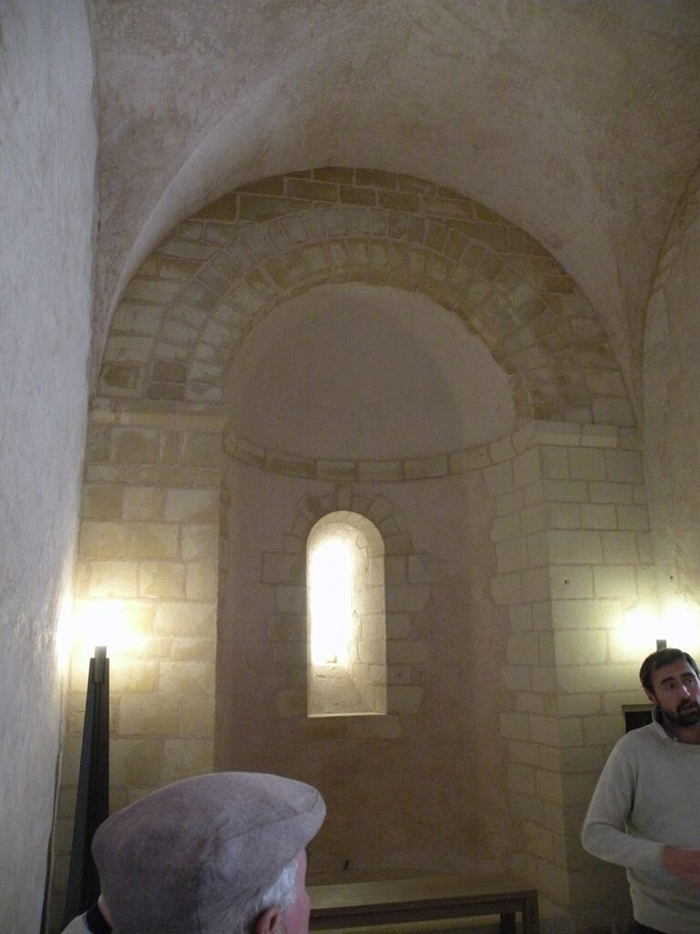 Château de Falaise 13 A small apsidal chapel at Chateau de Falaise, a semicircular apse under a half-dome framed by a round-headed arch and lit by one narrow window, with two visitors in the foreground.