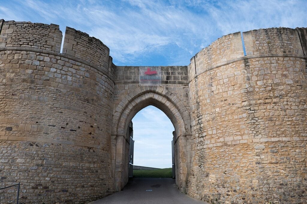 Château de Falaise 2 Looking out through the gate passage of Chateau de Falaise, a tall pointed arch with a massive round tower of coursed ashlar rising on each side and grass beyond.