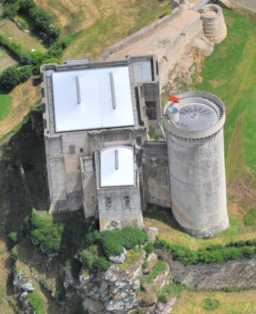 Château de Falaise 11 A near-vertical aerial of the keep block at Chateau de Falaise, the rectangular great tower under a pale modern roof, a smaller roofed block attached along one side, and a round tower at the corner, with rock and grass around them.