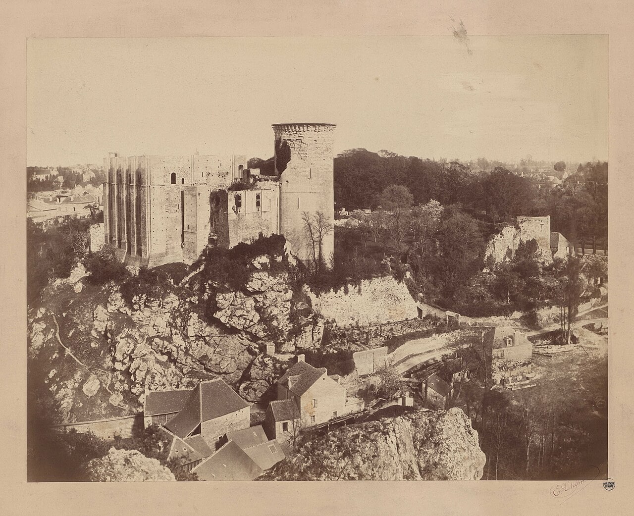 An 1877 photograph of Chateau de Falaise from across the valley, the great tower standing roofless behind its pilaster buttresses, the round Tour Talbot broken open near its top, and houses and walled gardens running up to the foot of the rock. An 1877 photograph of Chateau de Falaise from across the valley, the great tower standing roofless behind its pilaster buttresses, the round Tour Talbot broken open near its top, and houses and walled gardens running up to the foot of the rock.