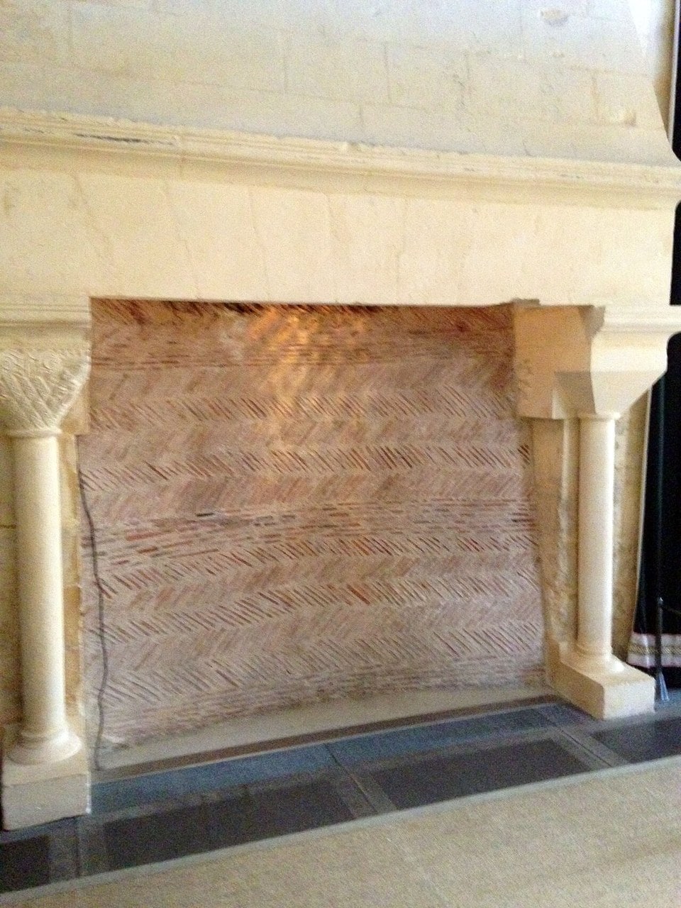 A wide stone fireplace in the small donjon at Chateau de Falaise, the back of its hearth laid in herringbone courses of thin flat stones, with a slender column and a carved capital at each side and crisply cut ashlar above. A wide stone fireplace in the small donjon at Chateau de Falaise, the back of its hearth laid in herringbone courses of thin flat stones, with a slender column and a carved capital at each side and crisply cut ashlar above.