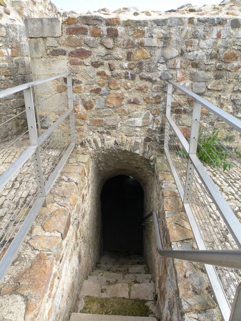 Château de Falaise 10 A flight of stone steps descending between modern white metal handrails into a dark vaulted opening within the rampart at Chateau de Falaise.