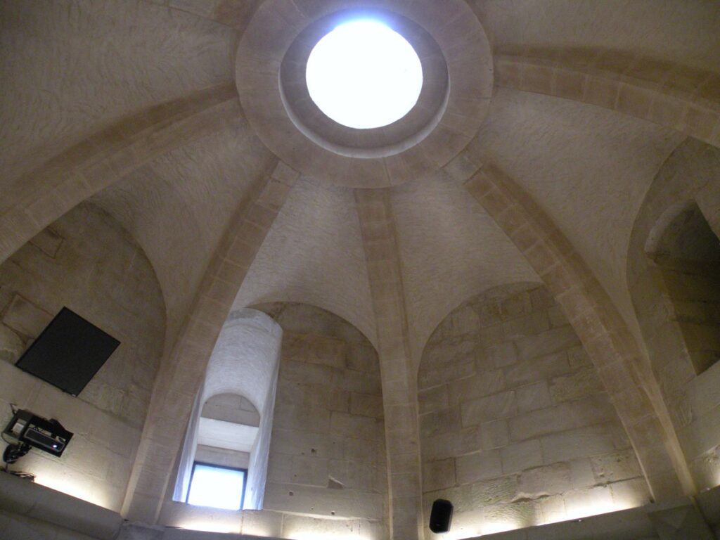 Château de Falaise 5 A ribbed stone vault inside the Tour Talbot at Chateau de Falaise with a circular opening at its centre letting in daylight, and tall narrow embrasures in the walls below.