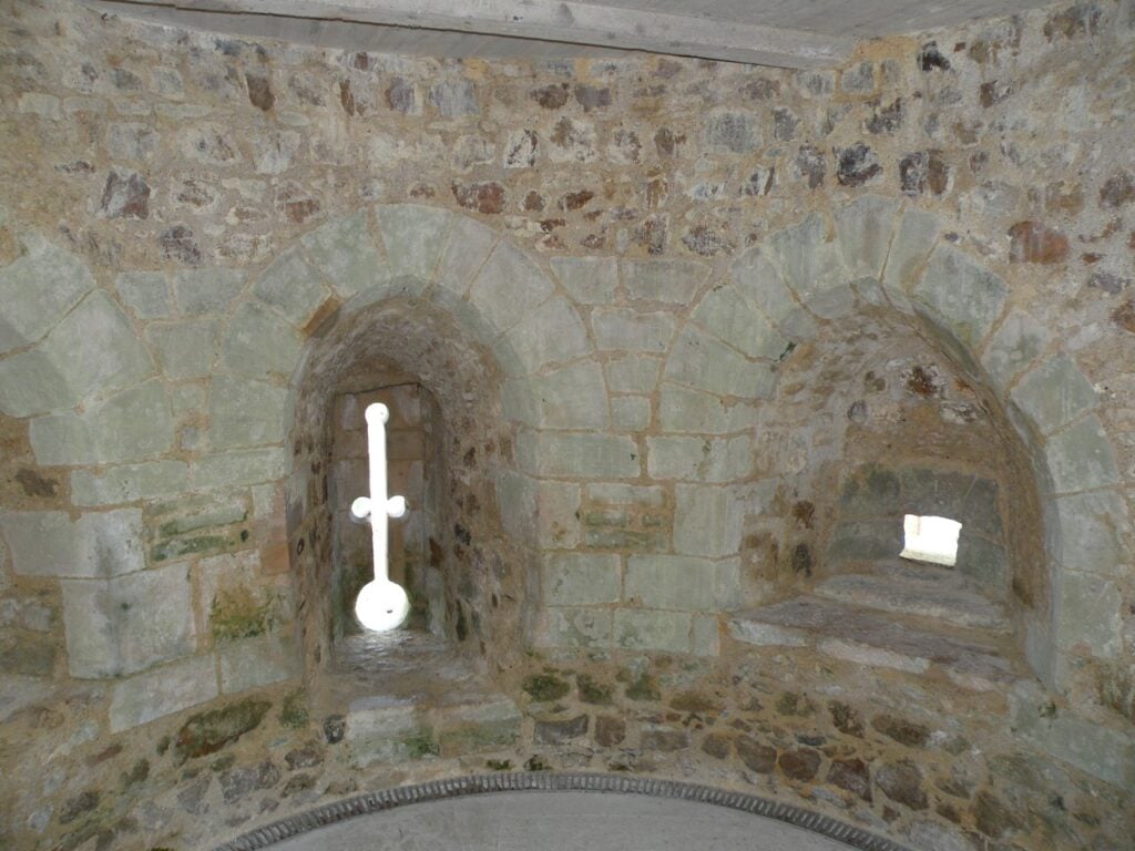 Château de Falaise 9 The inside of a vaulted chamber within a rampart at Chateau de Falaise, a cross-shaped loop with a round oillet letting light through the far face and a stone bench along the right side.