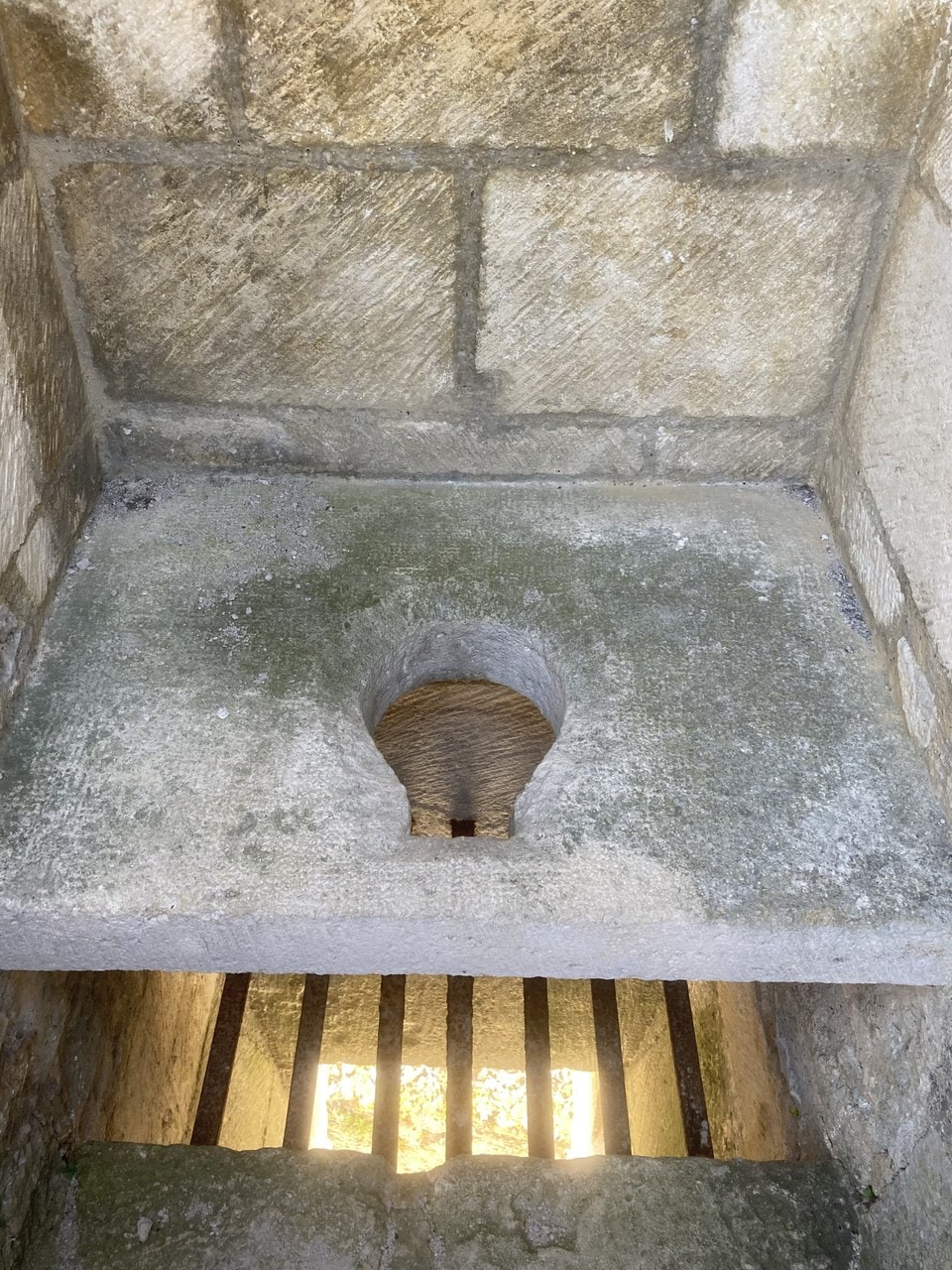 A stone bench built across a small vaulted chamber with a shaped opening cut through it; below and in front of the bench a barred grille opens onto daylight. A stone bench built across a small vaulted chamber with a shaped opening cut through it; below and in front of the bench a barred grille opens onto daylight.