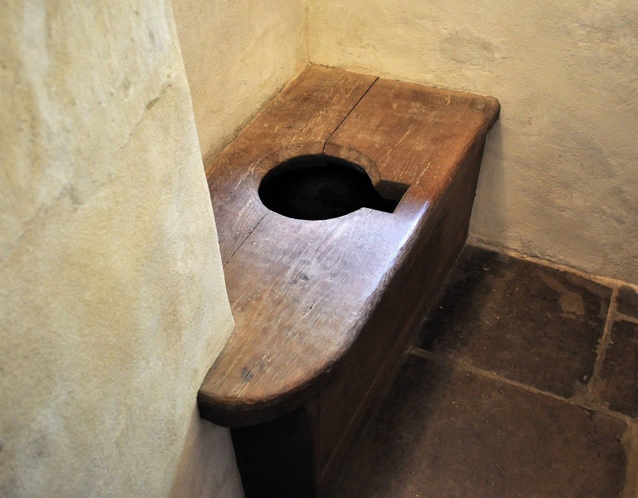 A heavy timber bench built along a plastered wall in a tiled room, with a large rounded opening cut through the boards. A heavy timber bench built along a plastered wall in a tiled room, with a large rounded opening cut through the boards.