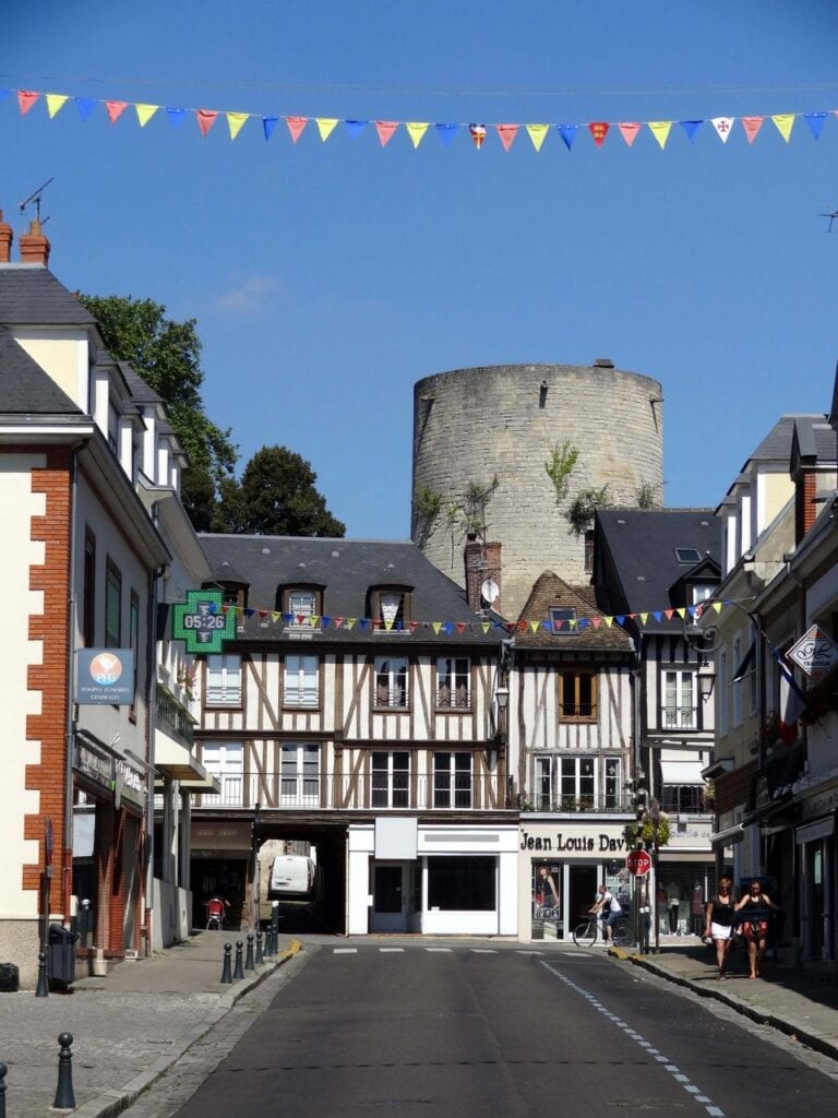 Château de Gisors 11 The roofless cylindrical great tower of Chateau de Gisors rising above the rooftops at the end of a town street lined with half-timbered houses, bunting strung across the street.