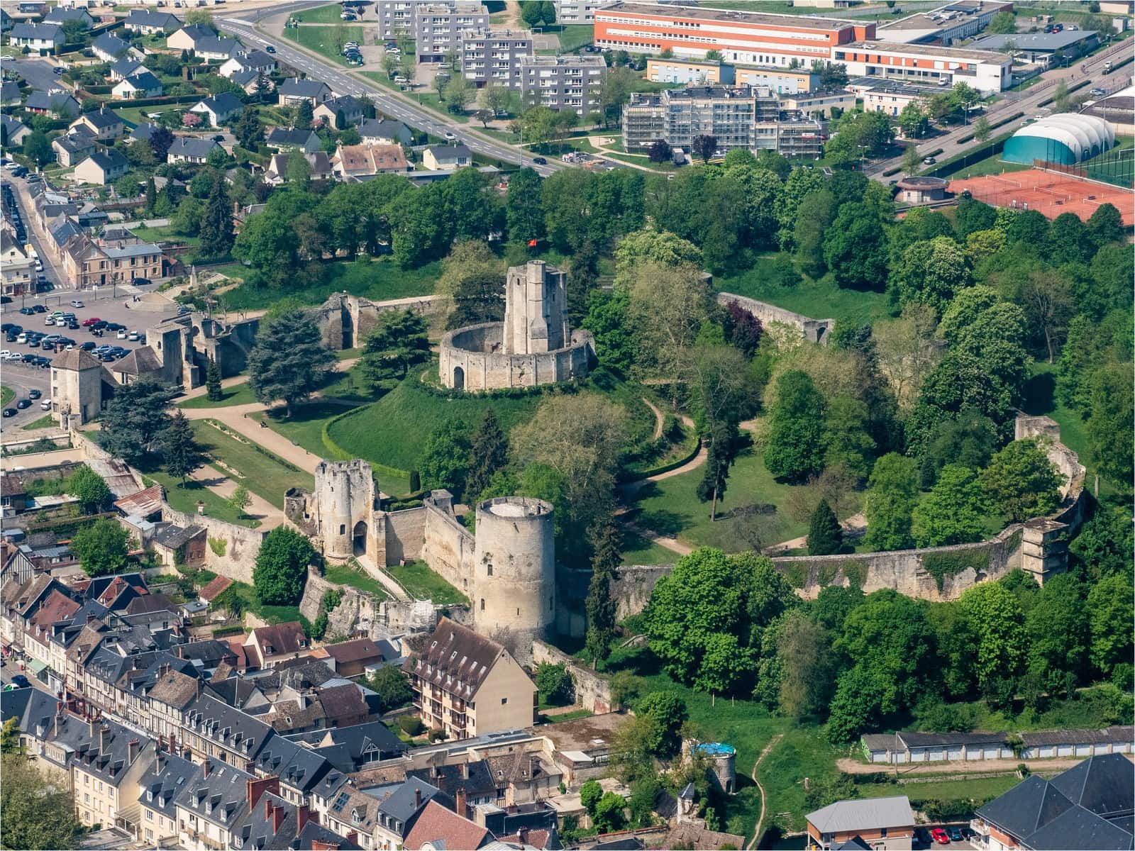 Château de Gisors 1 An oblique aerial view of Chateau de Gisors, the motte and its keep at the centre of a walled enclosure of parkland, with the town pressing against the walls on one side.