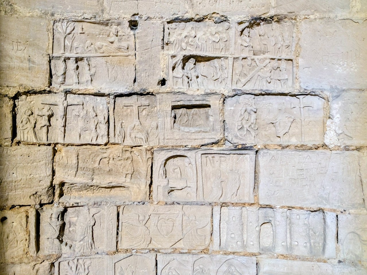 A wall of ashlar blocks in the Prisoner's Tower at Chateau de Gisors, each block carved with a separate small relief panel of figures, crosses and lettering. A wall of ashlar blocks in the Prisoner's Tower at Chateau de Gisors, each block carved with a separate small relief panel of figures, crosses and lettering.