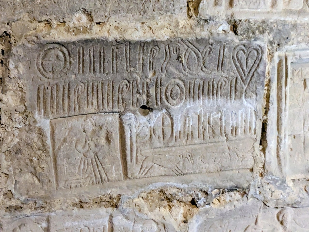 A carved panel in the Prisoner's Tower at Chateau de Gisors with two lines of deeply cut letters, a cross inside a circle, a heart, and small figure scenes beneath. A carved panel in the Prisoner's Tower at Chateau de Gisors with two lines of deeply cut letters, a cross inside a circle, a heart, and small figure scenes beneath.