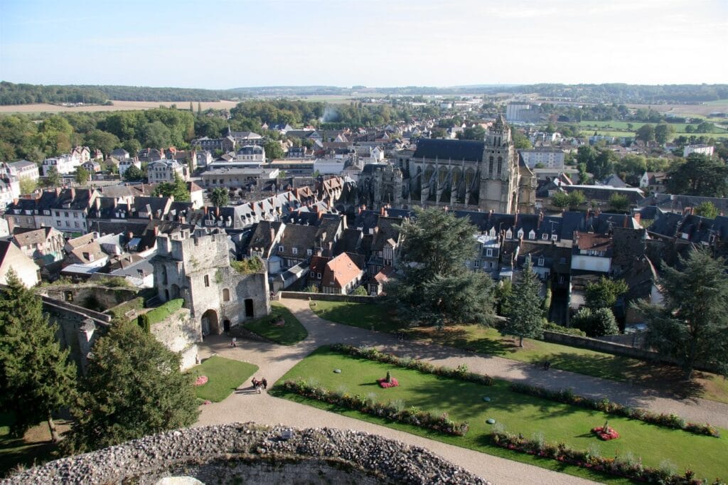 Château de Gisors 10 A high view from Chateau de Gisors over the lawns, gravel paths and flowerbeds of its park to the tiled and slate roofs of the town, a large Gothic church with a tall tower beyond and open farmland on the horizon.