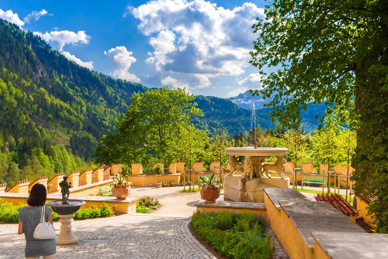 The terrace garden at Hohenschwangau Castle with a stone fountain, potted plants and a crenellated wall looking out over the wooded valley The terrace garden at Hohenschwangau Castle with a stone fountain, potted plants and a crenellated wall looking out over the wooded valley