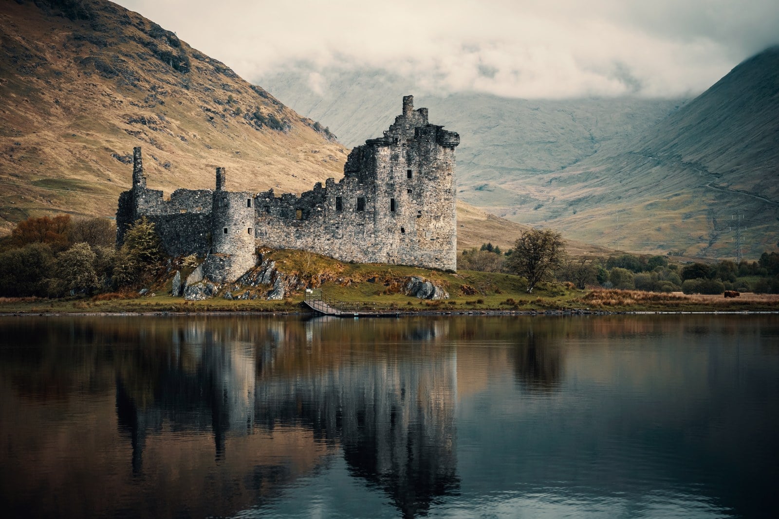 Kilchurn Castle 1 Kilchurn Castle standing roofless on a low green knoll at the head of Loch Awe, its tall tower house and long lower range mirrored in still water, with bare hills rising behind.