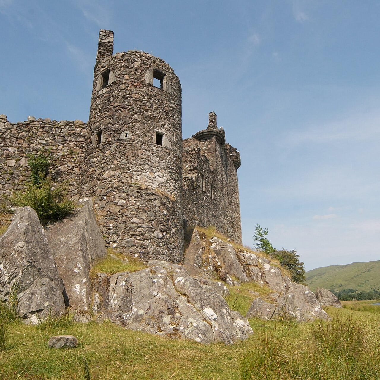 A round corner tower at Kilchurn Castle rising directly from a bare rock outcrop, with small square windows and narrow slit openings, and the tower house behind it. A round corner tower at Kilchurn Castle rising directly from a bare rock outcrop, with small square windows and narrow slit openings, and the tower house behind it.