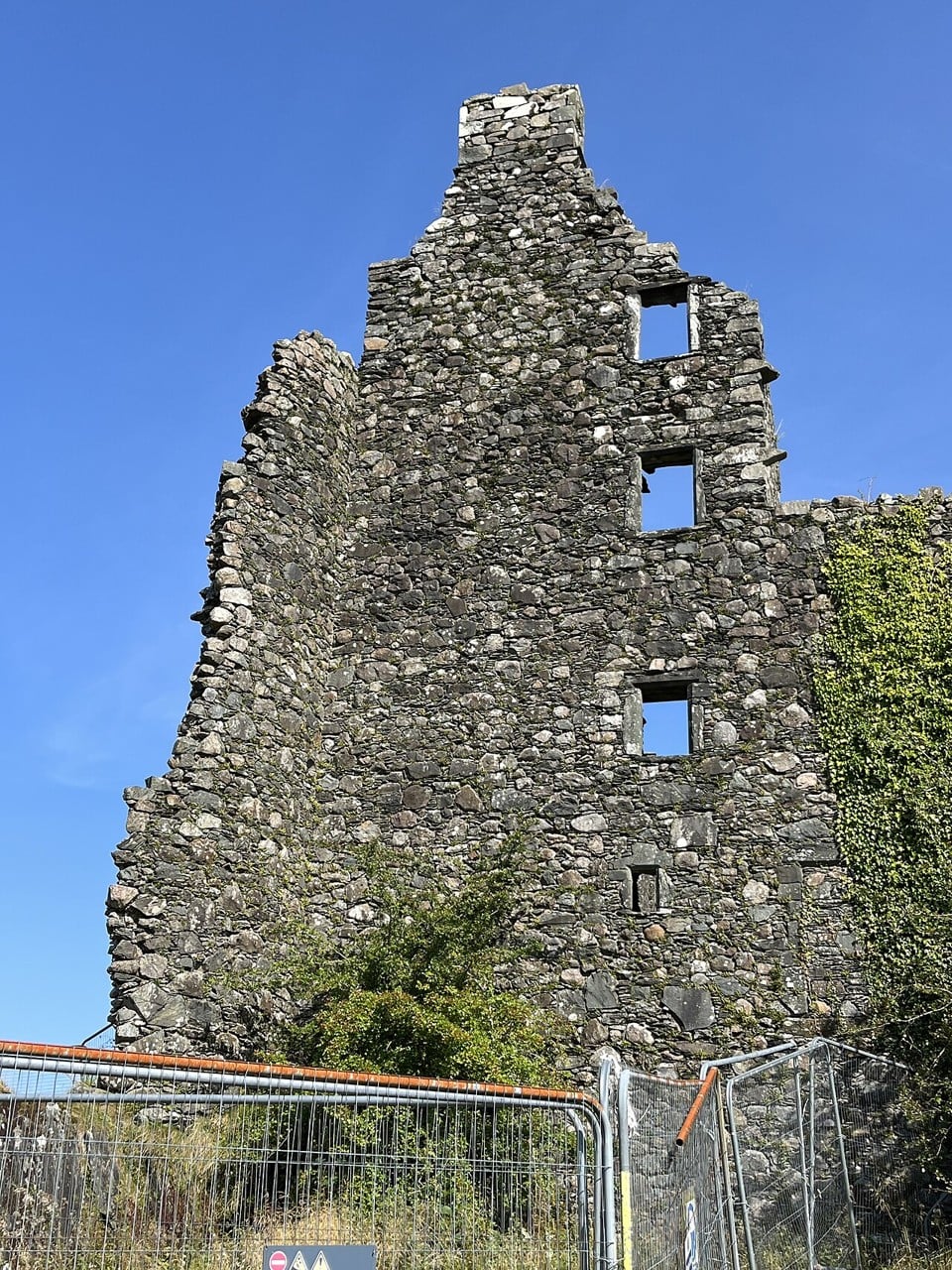 Temporary metal fence panels and a warning sign standing at the foot of a tall gable wall at Kilchurn Castle, photographed in September 2024. Temporary metal fence panels and a warning sign standing at the foot of a tall gable wall at Kilchurn Castle, photographed in September 2024.