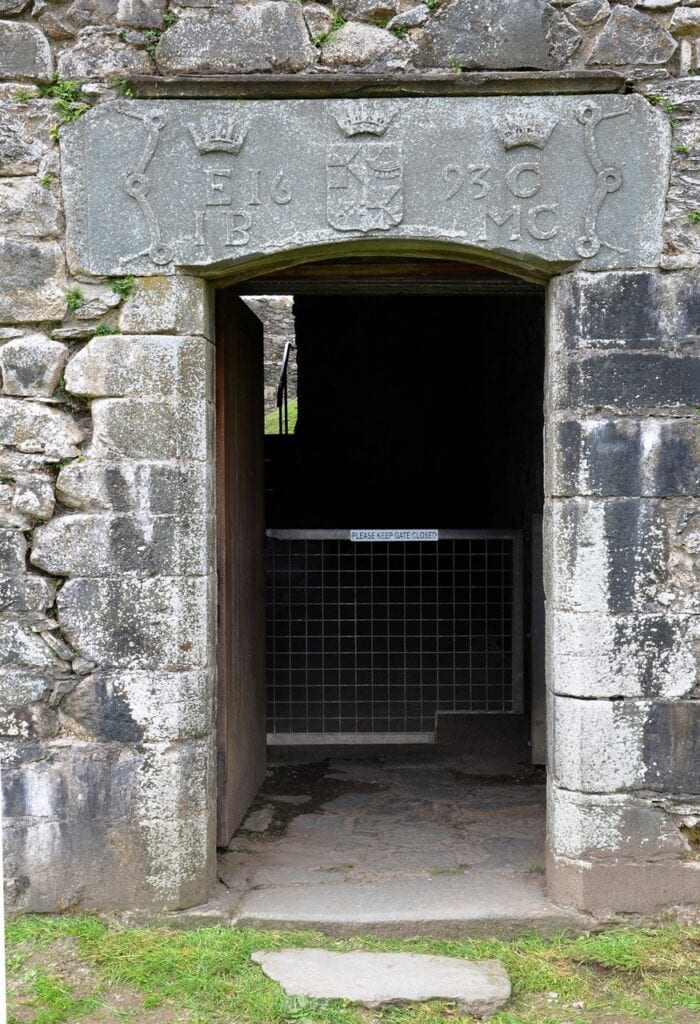 Kilchurn Castle 9 A stone doorway at Kilchurn Castle beneath a carved lintel bearing coronets, a shield and the date 1693, with a metal mesh gate closing the passage behind it.