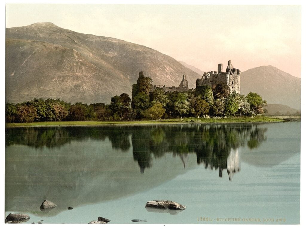 Kilchurn Castle 10 Photochrom print of Kilchurn Castle made between 1890 and 1900, the ruin standing among dense trees on the loch shore and reflected in still water.
