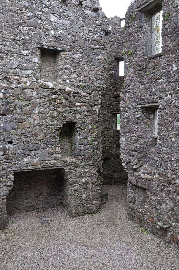 Kilchurn Castle 6 A wide stone fireplace in the wall of a roofless chamber at Kilchurn Castle, with two recesses in the masonry above it and a narrow passage running through to daylight beyond.