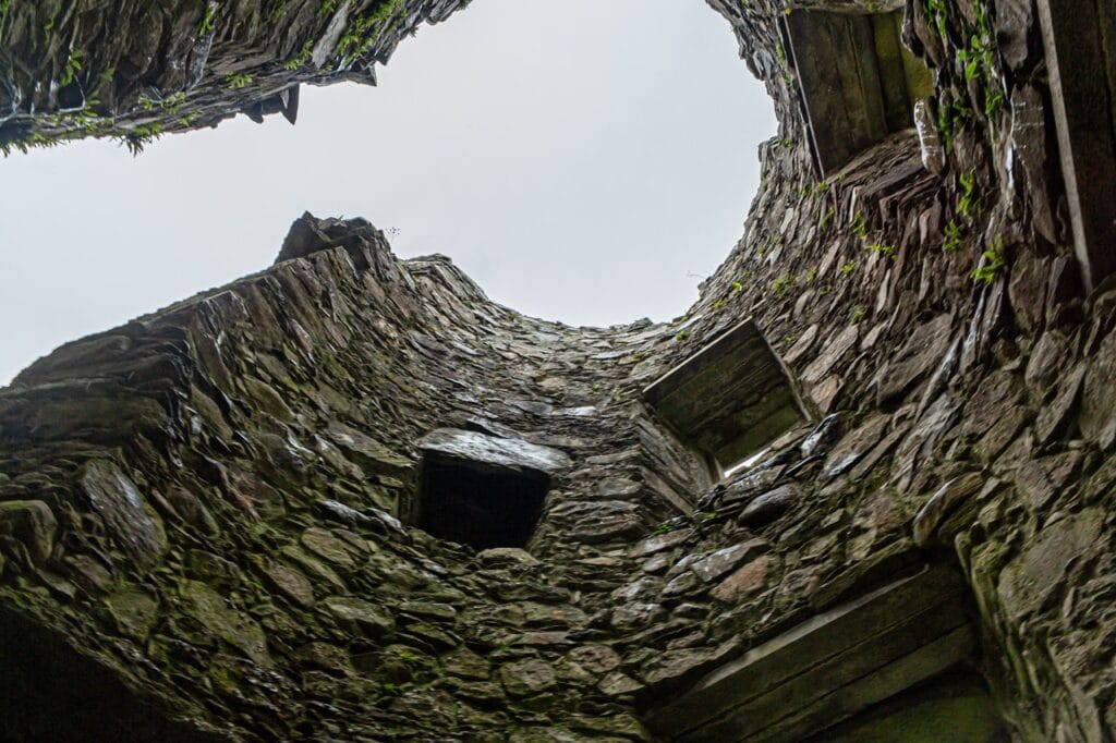 Kilchurn Castle 7 Steep upward view inside a roofless round tower at Kilchurn Castle, curved rubble walls rising to a broken wall-head against an overcast sky.