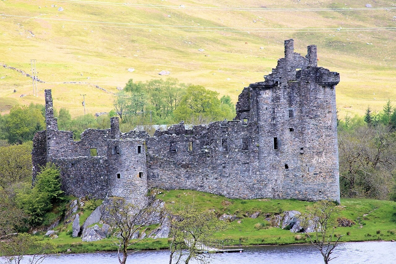 Kilchurn Castle seen across water from the landward side, with the tall roofless tower house at the right end and a long lower range extending to the left along the rock. Kilchurn Castle seen across water from the landward side, with the tall roofless tower house at the right end and a long lower range extending to the left along the rock.