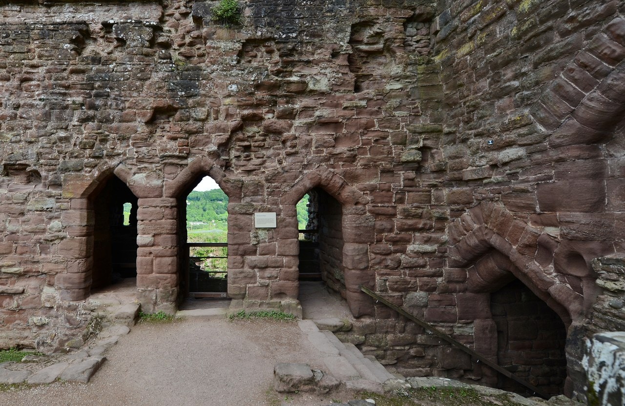 The interior of a red sandstone chamber with three pointed openings side by side in the far wall, daylight showing through the middle one, and rough stonework above and around. The interior of a red sandstone chamber with three pointed openings side by side in the far wall, daylight showing through the middle one, and rough stonework above and around.