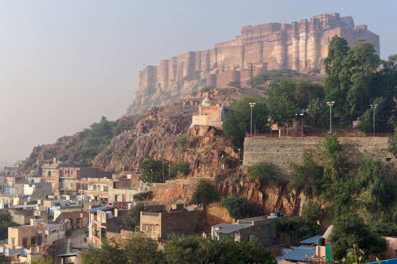 Mehrangarh stands on a sandstone cliff above Jodhpur, its ramparts rising straight out of the rock face, with the flat roofs and blue-washed walls of the city below at the left. Mehrangarh stands on a sandstone cliff above Jodhpur, its ramparts rising straight out of the rock face, with the flat roofs and blue-washed walls of the city below at the left.