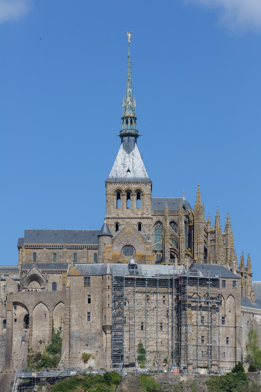 The abbey church and spire of Mont-Saint-Michel seen from below, above the tall buttressed wall of the Merveille The abbey church and spire of Mont-Saint-Michel seen from below, above the tall buttressed wall of the Merveille