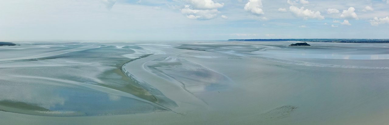 A wide panorama of sand flats and tidal channels in the bay under a pale sky A wide panorama of sand flats and tidal channels in the bay under a pale sky