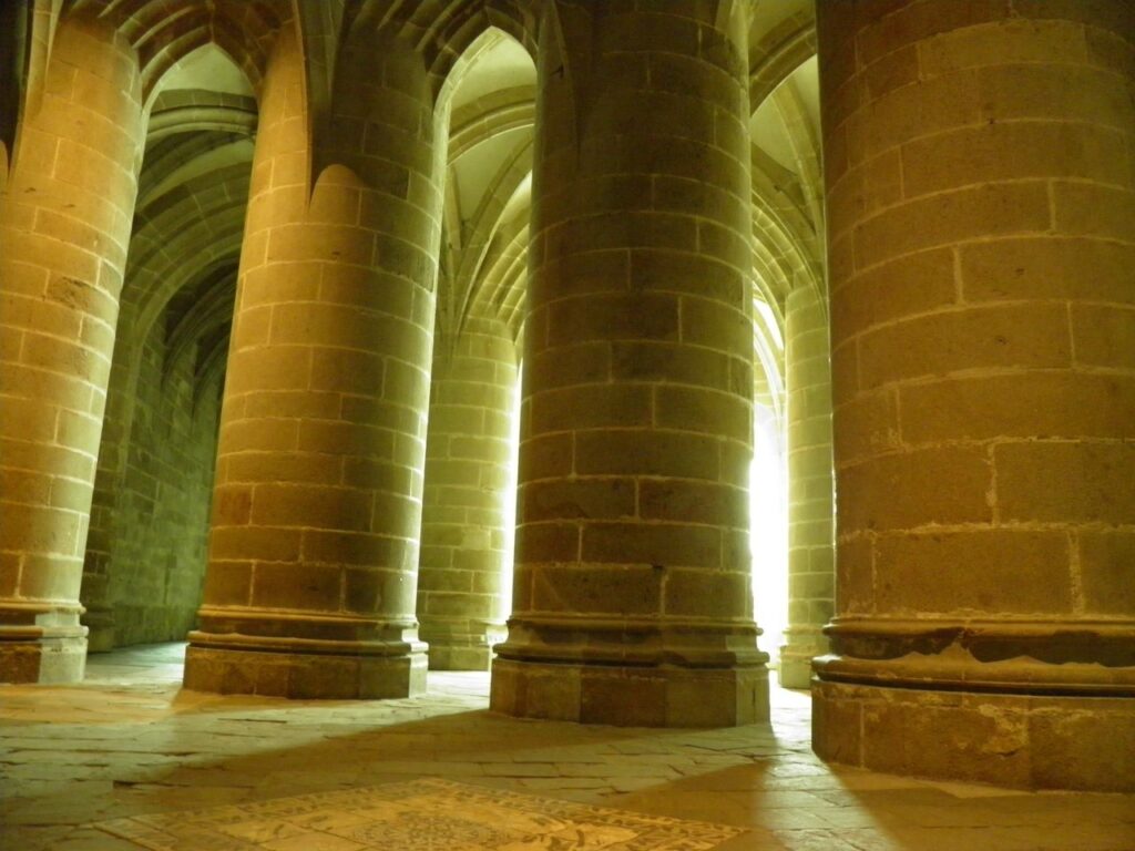 Mont-Saint-Michel 18 A crypt filled with massive round stone piers rising to ribbed vaults, lit in warm gold