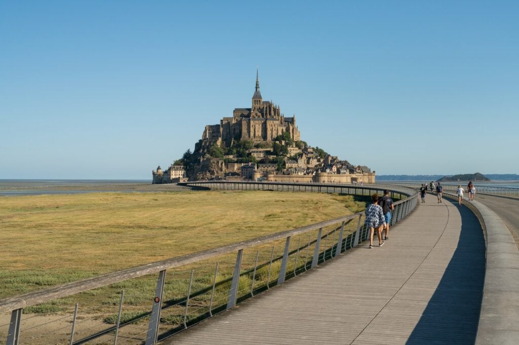 Mont-Saint-Michel 22 A long low footbridge with a railing running across grass and sand toward Mont-Saint-Michel