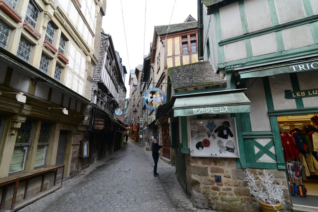 A narrow street between stone and timber-framed houses with shopfronts, climbing between the buildings A narrow street between stone and timber-framed houses with shopfronts, climbing between the buildings