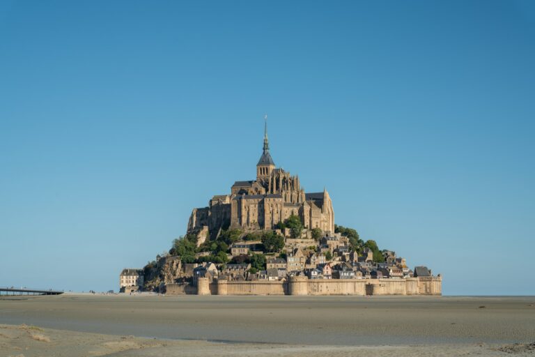 Home 8 Mont-Saint-Michel rising from wet sand flats at low tide, village roofs stacked below the abbey church and spire
