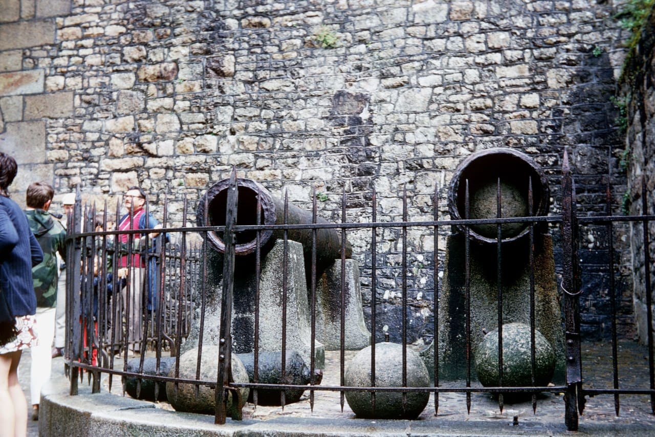 Two large iron bombards mounted in protective iron cages in front of a rubble stone wall Two large iron bombards mounted in protective iron cages in front of a rubble stone wall